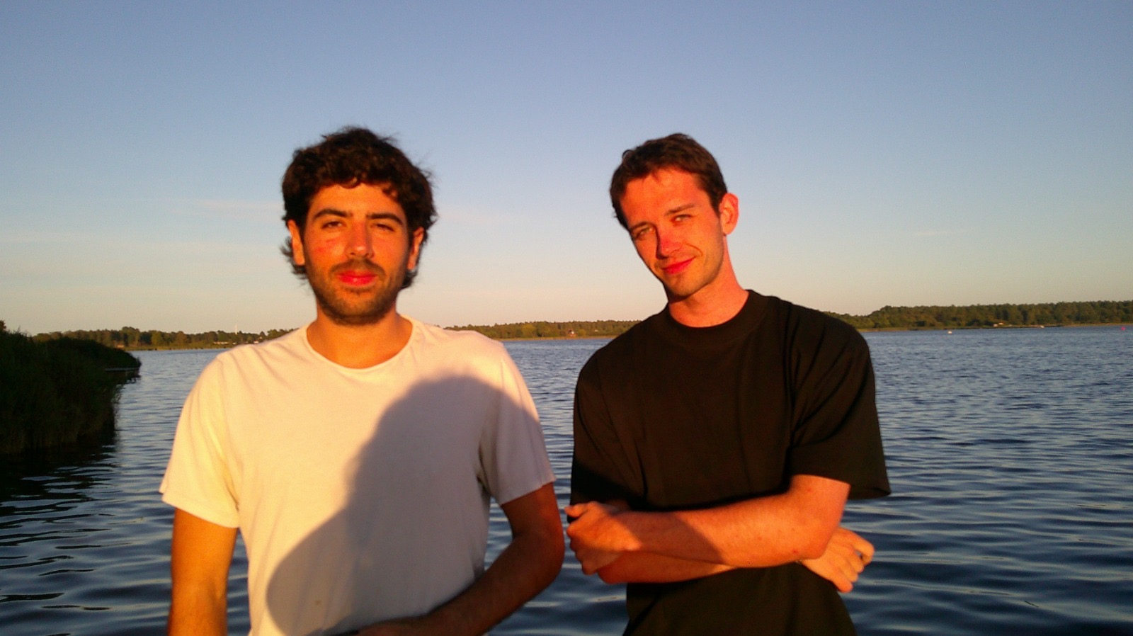 Two volunteers standing together beside the fjord in evening light
